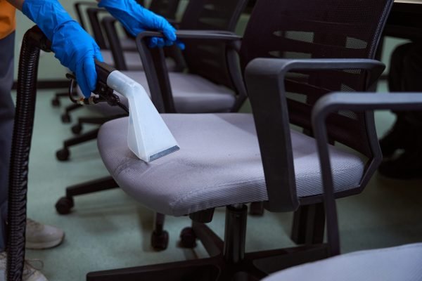 Cropped photo of janitor in rubber gloves cleaning the upholstery on chairs with vacuum-cleaner