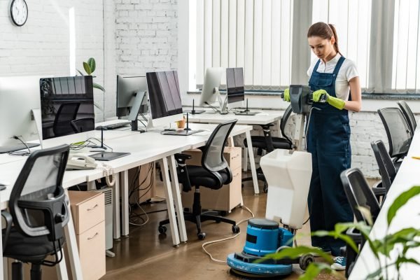 young cleaner washing floor in open space office with cleaning machine